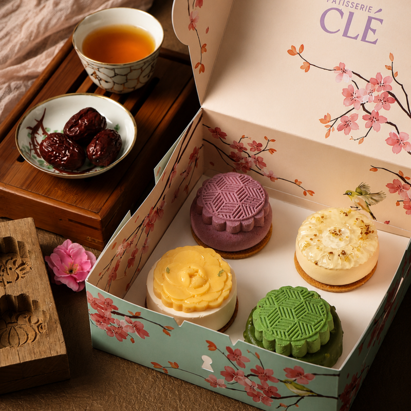 All four Pâtisserie CLÉ Mid-Autumn French Entremet Mooncakes - Chrysanthemum Yuzu, Mango Passionfruit, Orh Nee and Matcha - displayed on a plate alongside the gift box