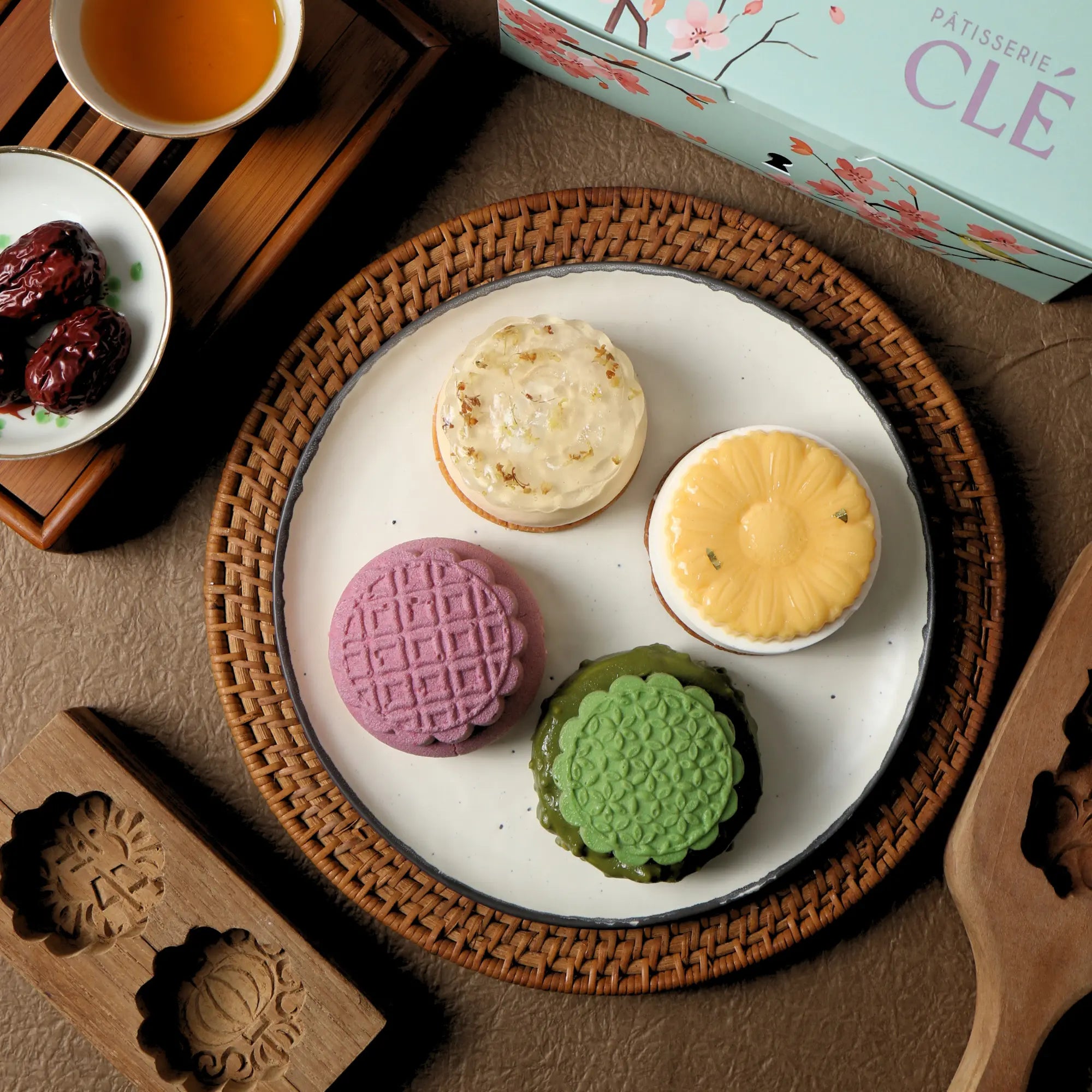 All four Mid Autumn entremet mooncakes displayed on a plate alongside the CLÉ gift box: Chrysanthemum Yuzu, Mango Passionfruit, Orh Nee, and Matcha.