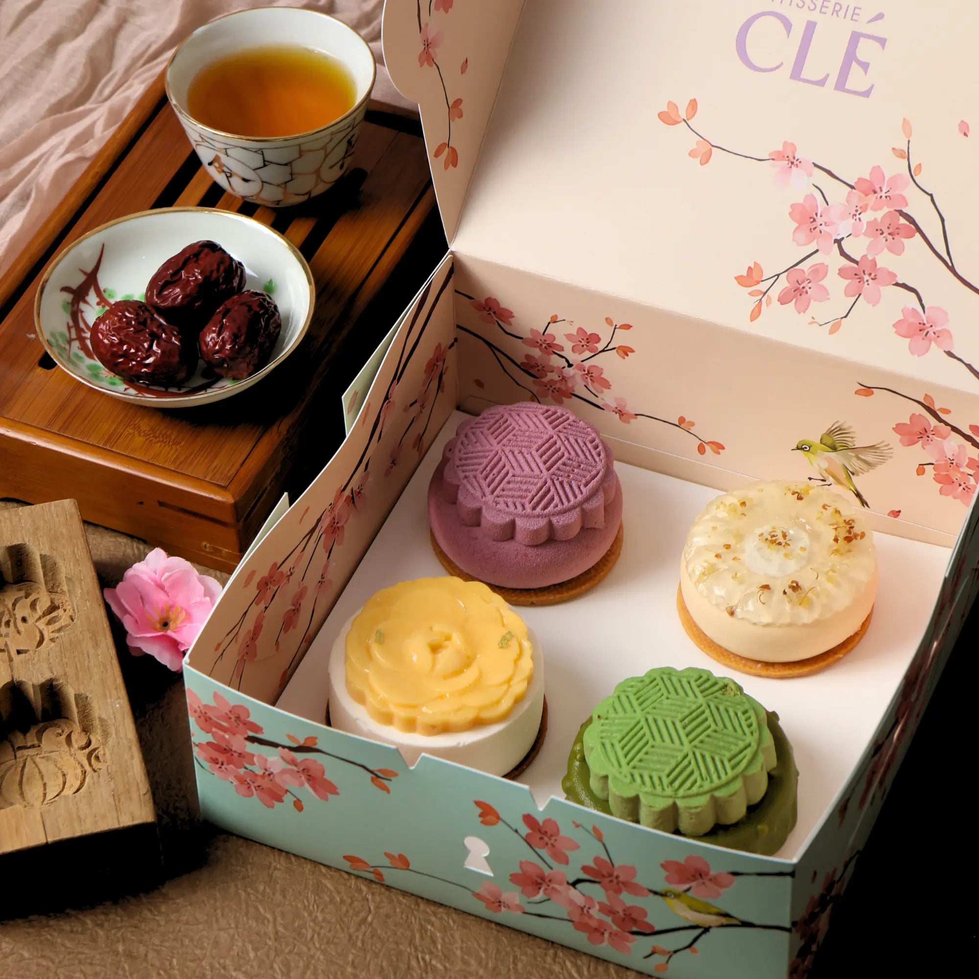 Four Mid Autumn Gift Box mooncakes displayed inside the open cherry blossom gift box, styled with tea and jujubes.